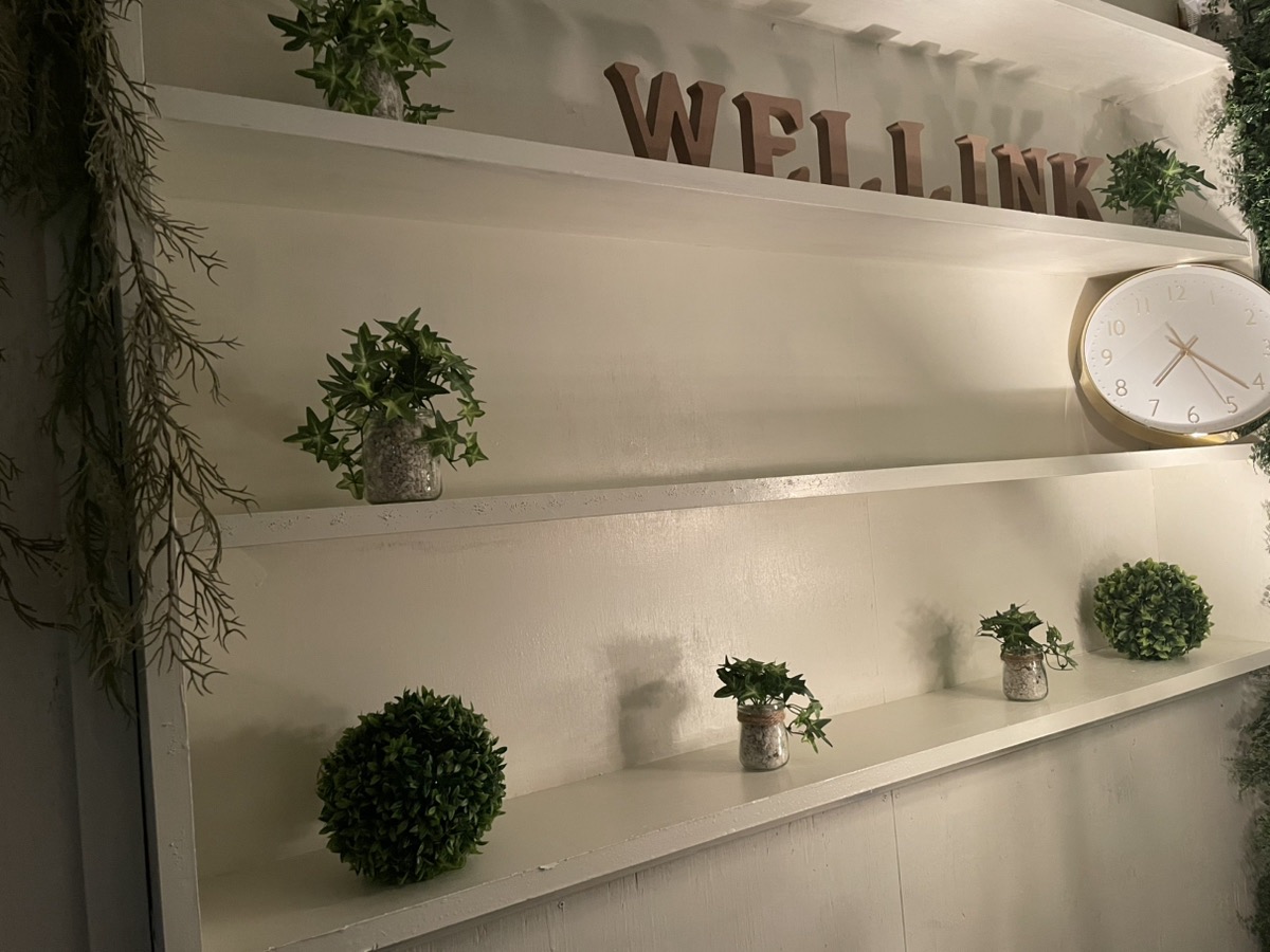 白い棚に観葉植物と時計、WELLINKの文字オブジェが飾られたインテリア